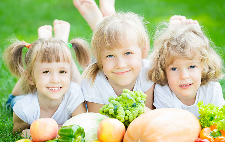 Three young girls laying on the grass with vegetables