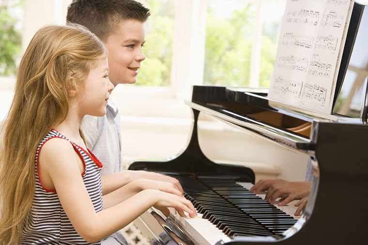 A boy and a girl smiling and playing a piano